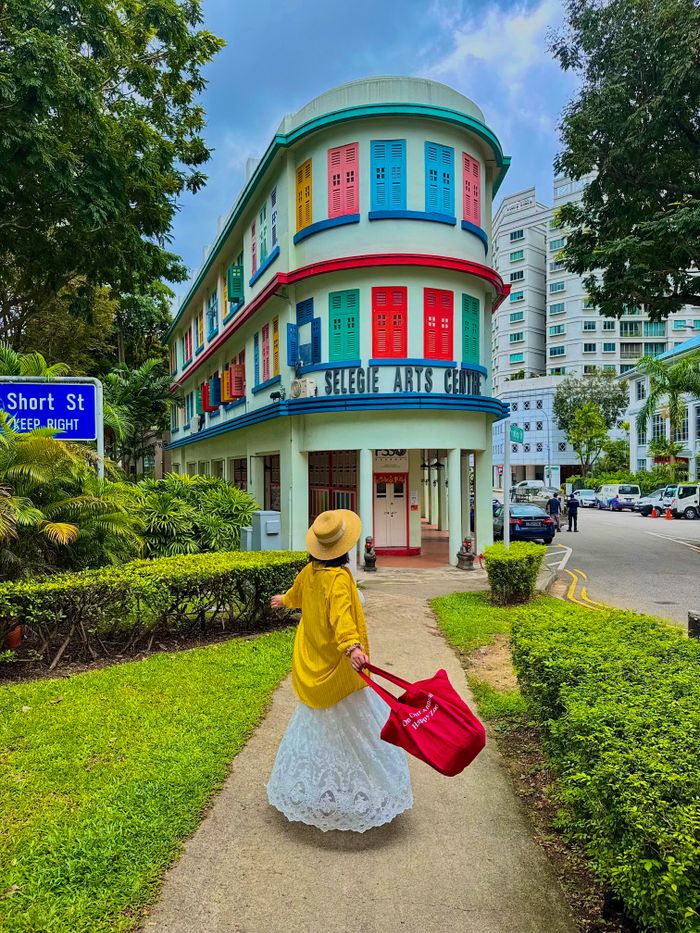 A woman in yellow walks by the vibrant Selegie Arts Centre in Singapore, an iconic colorful building.